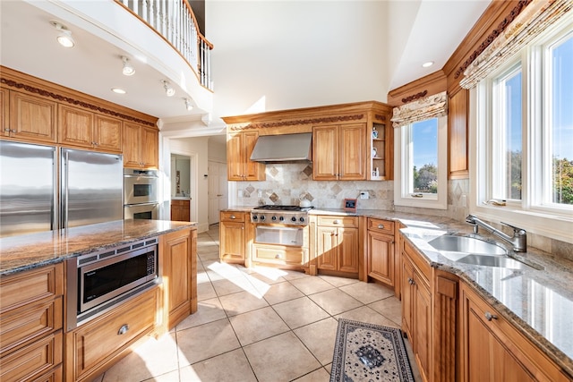 kitchen featuring plenty of natural light, backsplash, wall chimney exhaust hood, and built in appliances