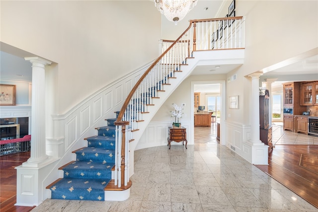 staircase with a chandelier, a high ceiling, decorative columns, and light wood-type flooring