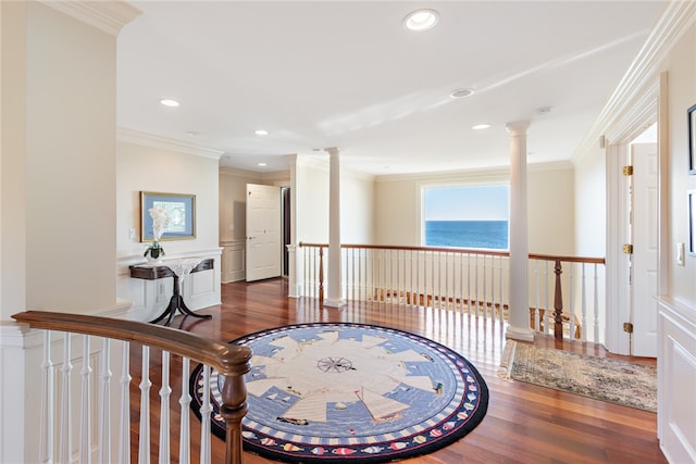 hallway featuring a water view, dark hardwood / wood-style floors, crown molding, and decorative columns