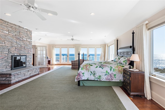 bedroom featuring a stone fireplace, dark hardwood / wood-style flooring, ceiling fan, and a water view