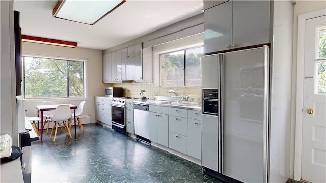 kitchen featuring a baseboard heating unit, appliances with stainless steel finishes, backsplash, sink, and dark tile floors