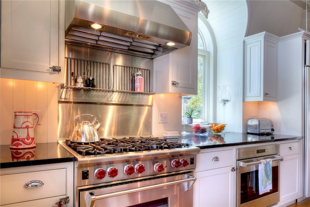 kitchen featuring stainless steel appliances, white cabinets, wall chimney exhaust hood, and tasteful backsplash