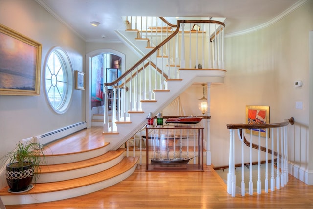 stairway with a baseboard heating unit, crown molding, and wood-type flooring