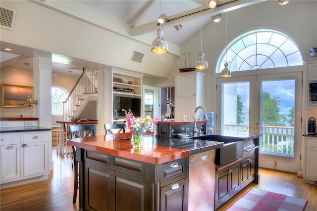 kitchen featuring light hardwood / wood-style flooring, an island with sink, decorative light fixtures, dark brown cabinetry, and white cabinets