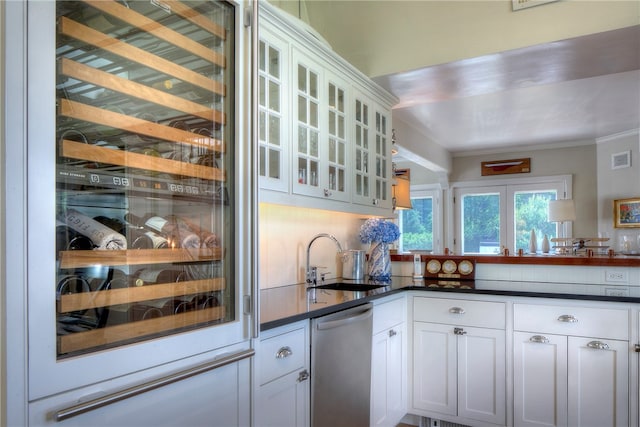 kitchen with beverage cooler, tasteful backsplash, stainless steel dishwasher, sink, and white cabinets