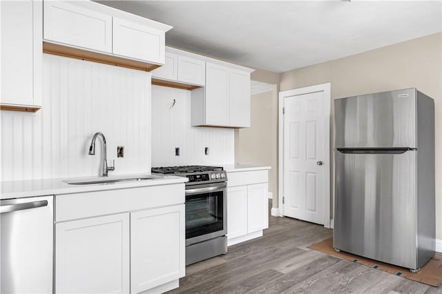 kitchen with stainless steel appliances, a sink, white cabinets, light countertops, and light wood-type flooring