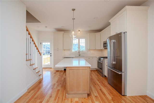 kitchen with a kitchen island, light wood-type flooring, stainless steel appliances, hanging light fixtures, and white cabinetry