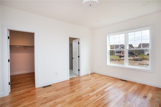 unfurnished bedroom featuring a closet, light hardwood / wood-style floors, a walk in closet, and ensuite bath