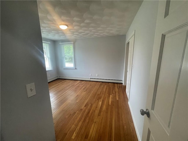 unfurnished room with a baseboard heating unit and wood-type flooring