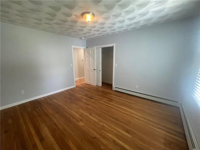 unfurnished bedroom featuring a baseboard radiator, wood-type flooring, and a closet