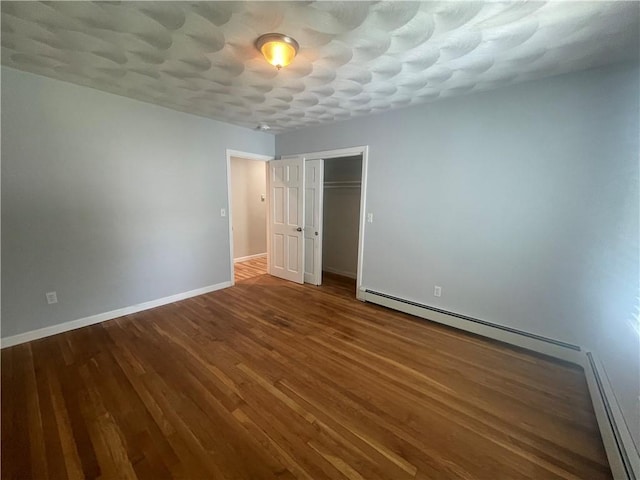 unfurnished bedroom featuring a baseboard heating unit, wood-type flooring, and a closet