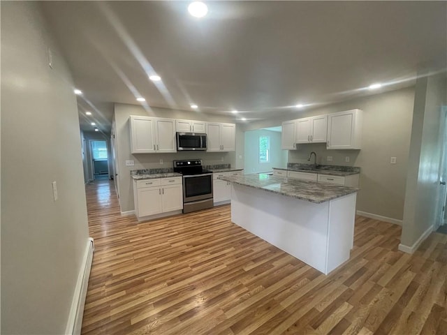 kitchen featuring sink, light stone counters, light wood-type flooring, appliances with stainless steel finishes, and white cabinets