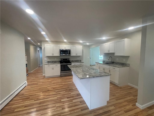 kitchen featuring sink, white cabinetry, baseboard heating, stainless steel appliances, and light stone countertops