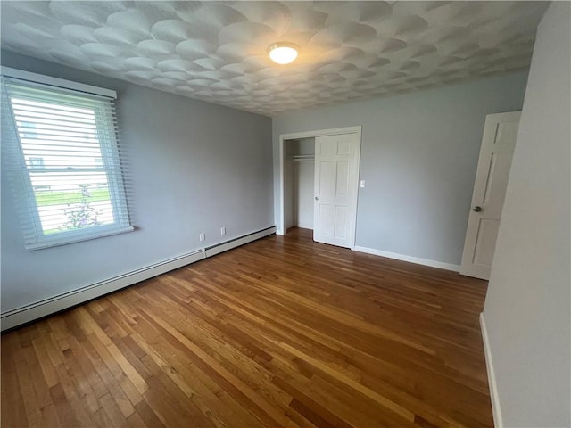 unfurnished bedroom with hardwood / wood-style floors, a closet, and a baseboard heating unit