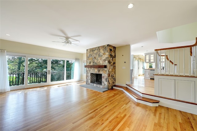 unfurnished living room featuring light hardwood / wood-style floors, a stone fireplace, and ceiling fan