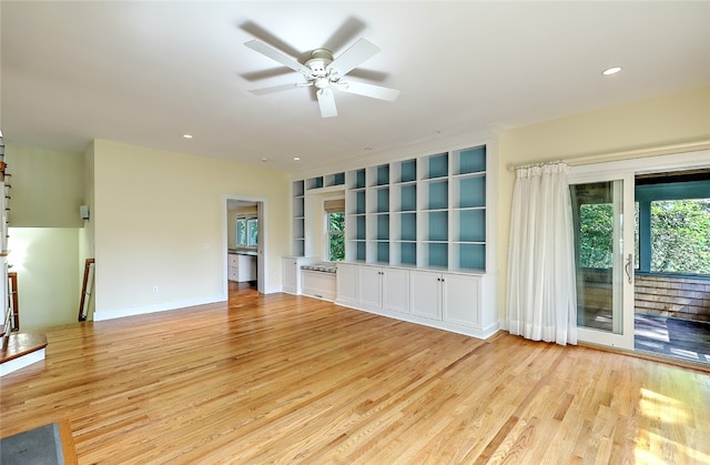 unfurnished living room featuring built in shelves, ceiling fan, and light wood-type flooring