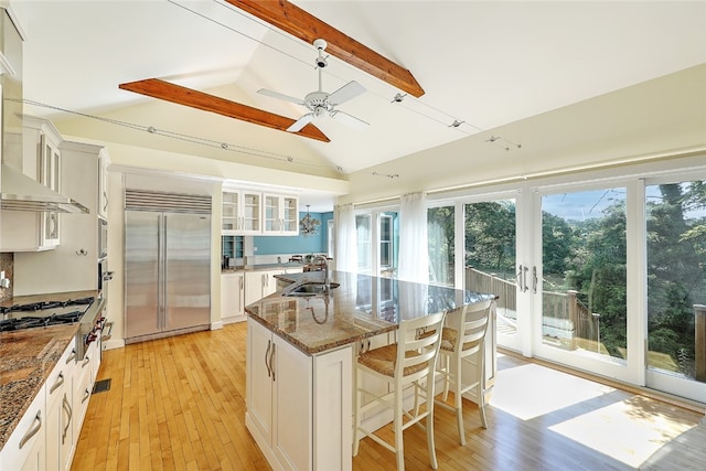 kitchen featuring lofted ceiling with beams, stainless steel built in fridge, light hardwood / wood-style flooring, and an island with sink