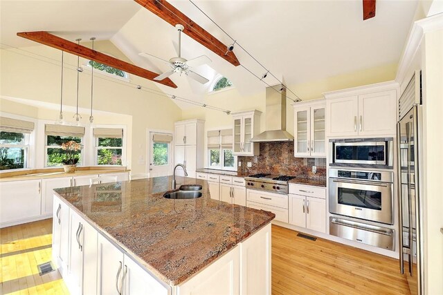 kitchen featuring built in appliances, sink, white cabinets, and wall chimney exhaust hood