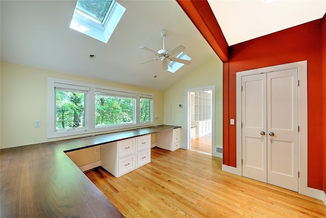 unfurnished office with light hardwood / wood-style floors, vaulted ceiling with skylight, ceiling fan, and built in desk