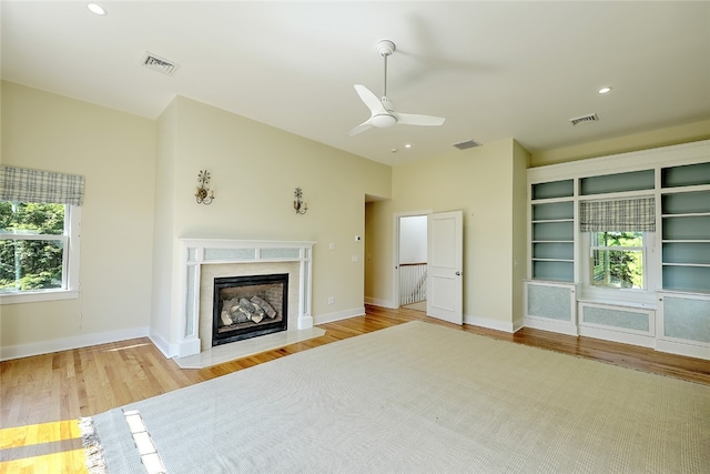 unfurnished living room featuring light hardwood / wood-style floors, a fireplace, ceiling fan, and built in shelves