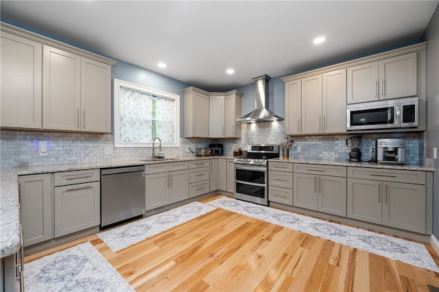 kitchen featuring gray cabinetry, wall chimney range hood, sink, stainless steel appliances, and light hardwood / wood-style flooring