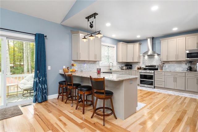 kitchen featuring wall chimney exhaust hood, a breakfast bar area, kitchen peninsula, stainless steel appliances, and decorative light fixtures