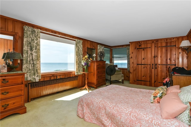 carpeted bedroom with radiator heating unit, a water view, and wood walls