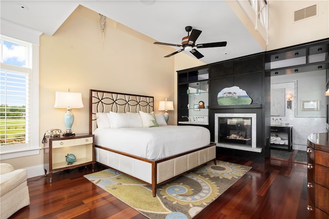 bedroom featuring ceiling fan, a high ceiling, a multi sided fireplace, and dark wood-type flooring