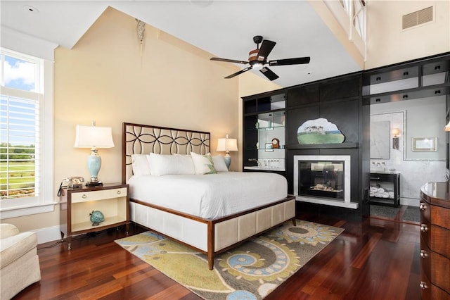 bedroom featuring wood finished floors, a glass covered fireplace, baseboards, and visible vents