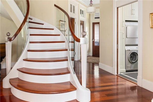staircase featuring baseboards, stacked washer / dryer, and wood finished floors