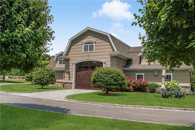view of front of property featuring an attached garage, a front yard, a gambrel roof, driveway, and a shingled roof