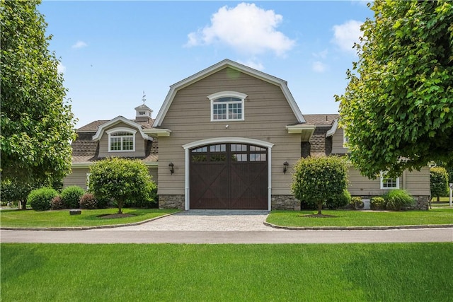 dutch colonial featuring stone siding, a front yard, a gambrel roof, roof with shingles, and driveway