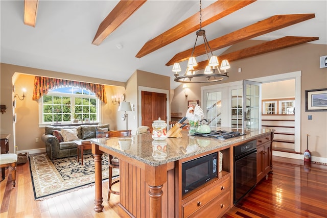 kitchen with black appliances, hardwood / wood-style floors, light stone counters, hanging light fixtures, and a center island