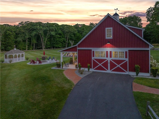 outdoor structure at dusk featuring an outbuilding, aphalt driveway, a barn, a gazebo, and a yard