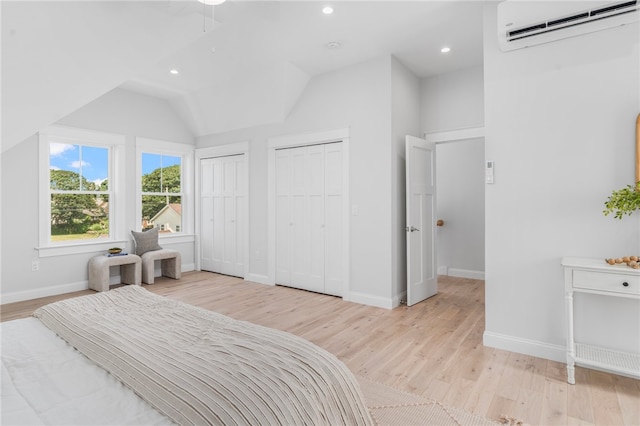 bedroom featuring lofted ceiling, two closets, light hardwood / wood-style floors, and an AC wall unit