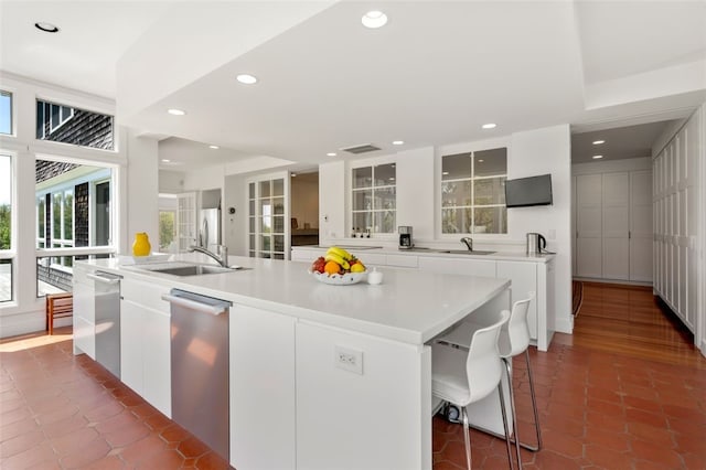 kitchen with stainless steel dishwasher, white cabinetry, tile patterned floors, sink, and a center island with sink