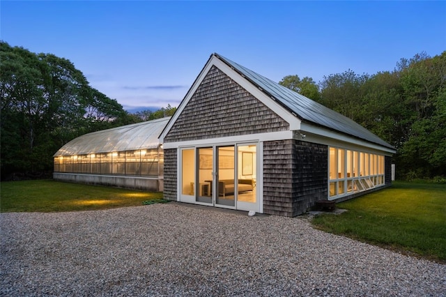 back house at dusk with an outdoor structure and a lawn