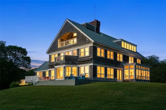 back house at dusk featuring a balcony and a lawn