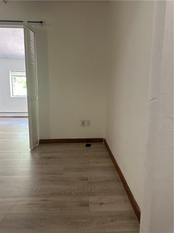 unfurnished room with hardwood / wood-style flooring and a baseboard heating unit