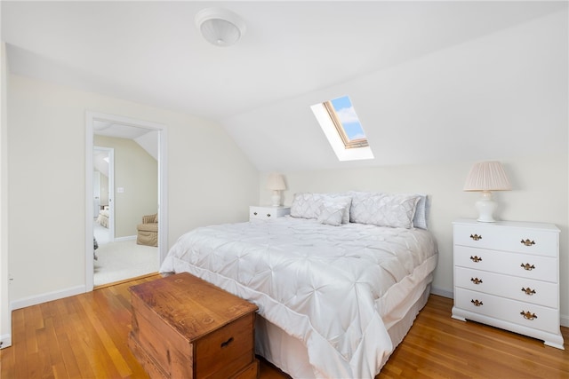 bedroom featuring light wood-type flooring, vaulted ceiling with skylight, and ensuite bath