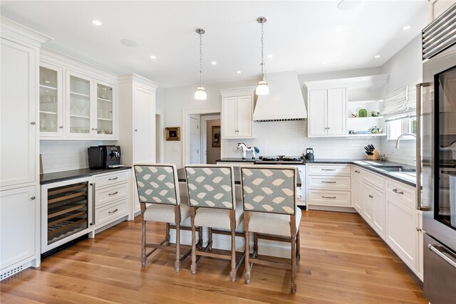 kitchen featuring light wood-type flooring, sink, beverage cooler, hanging light fixtures, and custom range hood