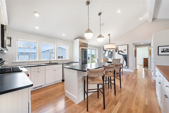 kitchen with light wood-type flooring, a center island, sink, white cabinetry, and hanging light fixtures