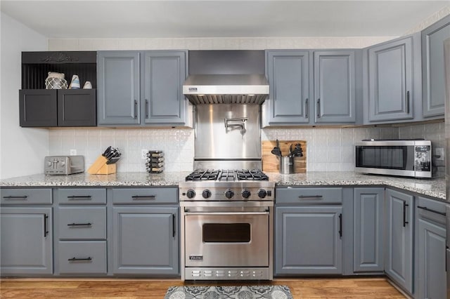 kitchen featuring light stone countertops, appliances with stainless steel finishes, backsplash, and wall chimney exhaust hood