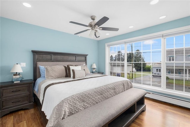 bedroom featuring ceiling fan, hardwood / wood-style floors, and a baseboard heating unit