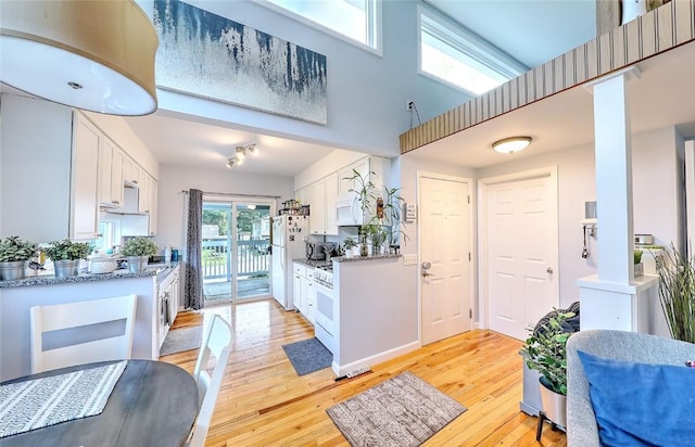 kitchen featuring white appliances, light stone countertops, light hardwood / wood-style flooring, a high ceiling, and white cabinetry