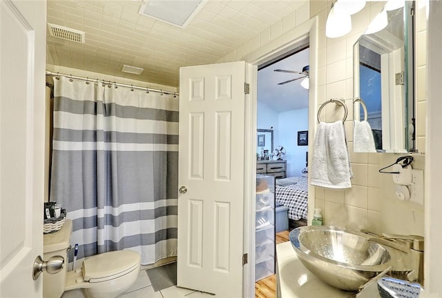 bathroom featuring toilet, tile walls, ceiling fan, and curtained shower