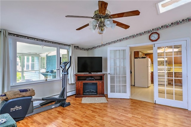 workout area with a skylight, light wood-type flooring, ceiling fan, french doors, and a baseboard heating unit