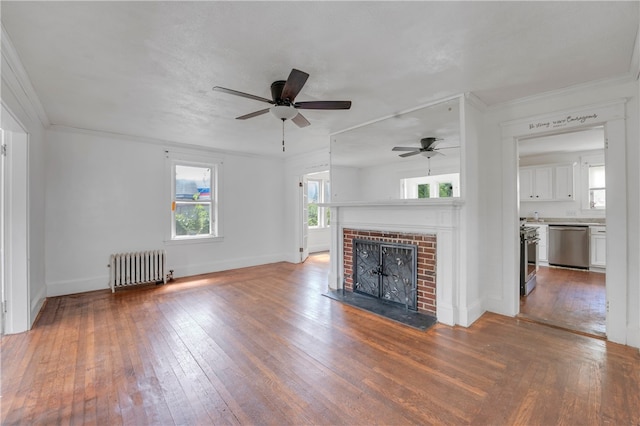 unfurnished living room with crown molding, a brick fireplace, wood-type flooring, ceiling fan, and radiator