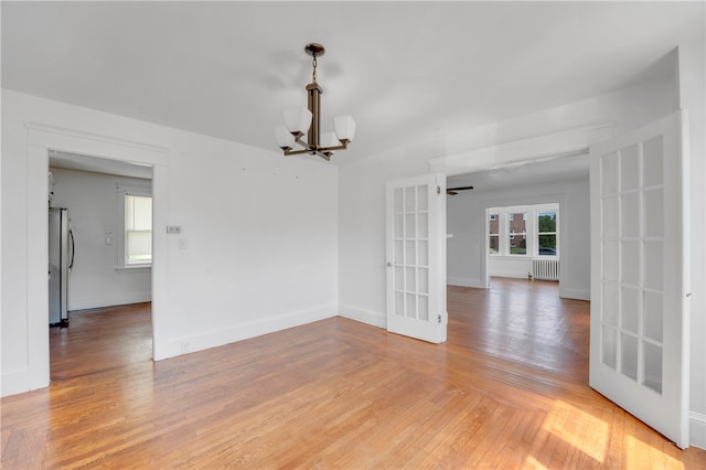 unfurnished room with radiator heating unit, wood-type flooring, french doors, and a chandelier