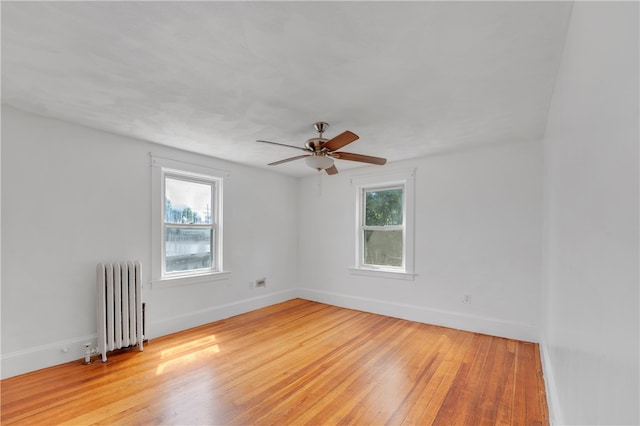 empty room with ceiling fan, radiator, light hardwood / wood-style flooring, and a wealth of natural light